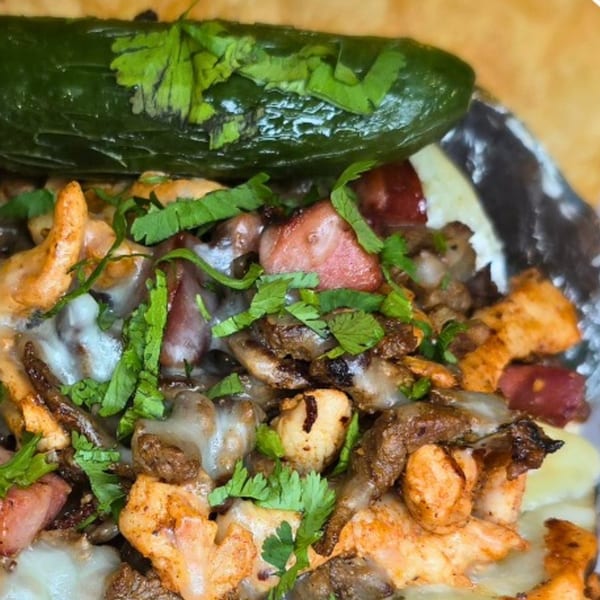 Close-up of Rey del Pollo's Mexican dish with meat, melted cheese, cilantro, and a whole jalapeño.