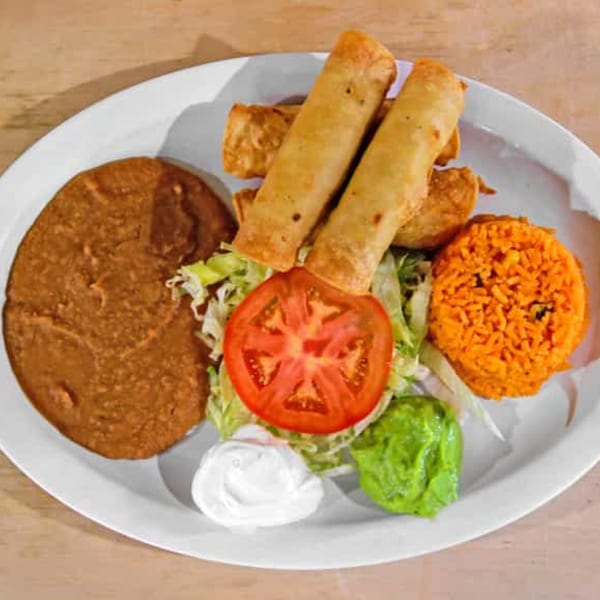 Rey del Pollo's Mexican dish with taquitos, refried beans, rice, lettuce, tomato, sour cream, and guacamole.