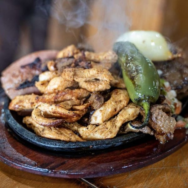 Sizzling Rey del Pollo fajitas with chicken, steak, grilled onion, and a jalapeño on a hot plate.
