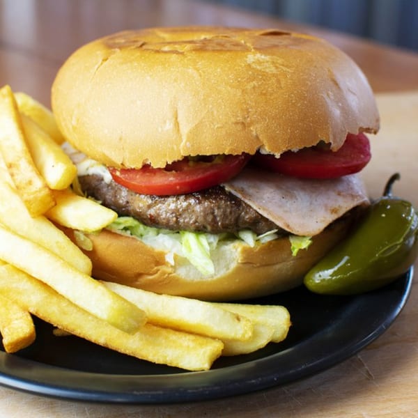 A Rey del Pollo burger with fries and a pickled jalapeño on a black plate.