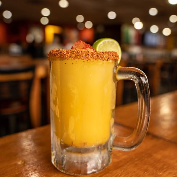 A Rey del Pollo mango margarita with chili-lime rim, garnished with lime and strawberry.