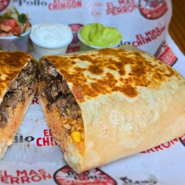 A large Rey del Pollo burrito, cut in half, revealing meat, rice, and corn, with sides of salsa and guacamole.