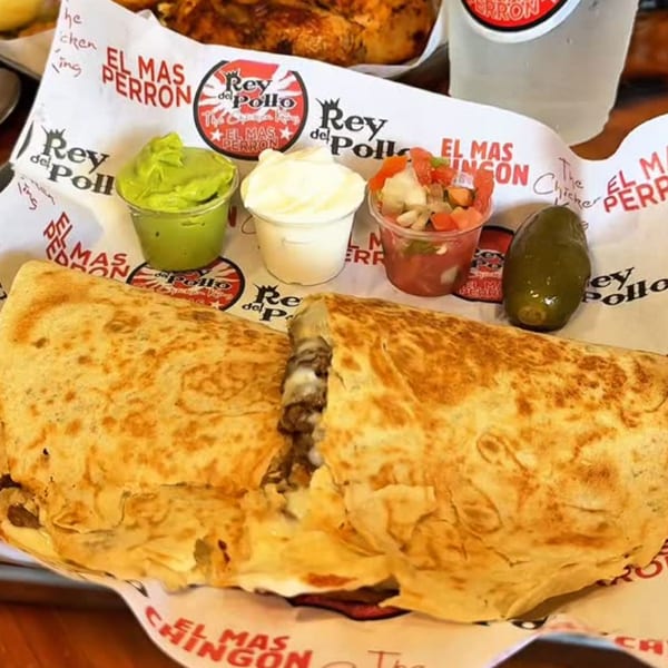 A large quesadilla with meat and cheese, served with guacamole, sour cream, salsa, and a jalapeño.